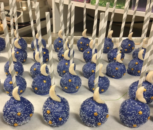 Blue cake pops decorated with white crescent moons and yellow stars, placed on striped straws.