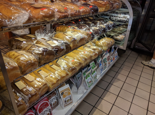 A display of various types of bread, including loaves and packaged goods, in a bakery setting.