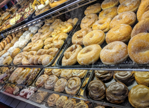 A display case filled with a variety of freshly baked donuts and pastries, showcasing different shapes and toppings.
