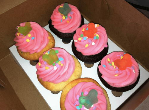A box of six cupcakes with pink frosting, colorful sprinkles, and gummy butterfly toppers.