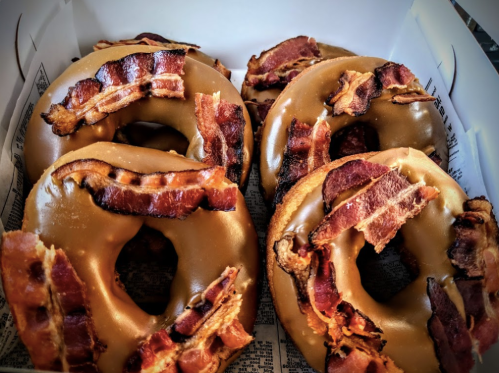 A box of donuts topped with caramel glaze and crispy bacon strips.