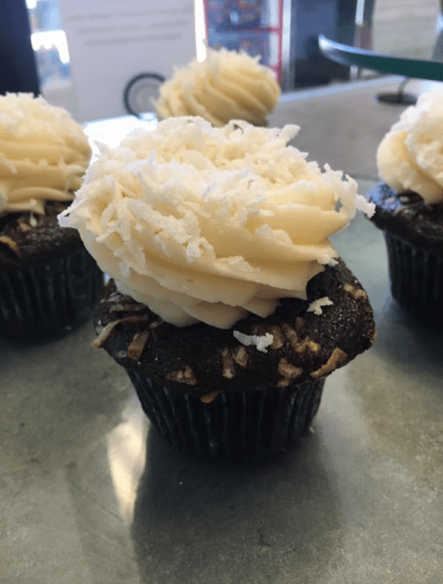 A chocolate cupcake topped with creamy white frosting and shredded coconut, placed on a green countertop.