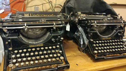 Two vintage Underwood typewriters on a wooden surface, one partially covered with a black cloth.