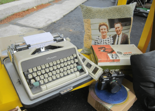 A vintage typewriter, a photo of a couple, a camera, and a box labeled "HEAT MARGARINE" on a table.