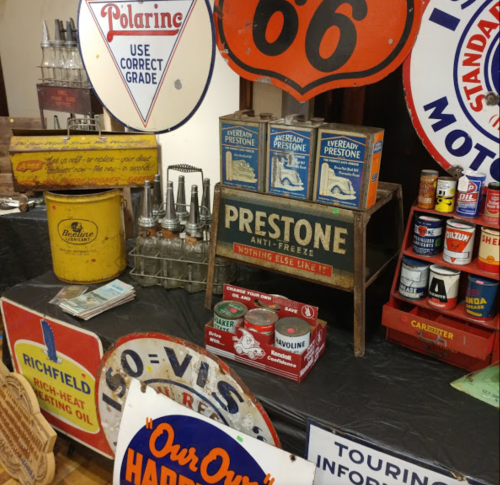 A display of vintage automotive signs and products, including Prestone antifreeze and various oil cans.