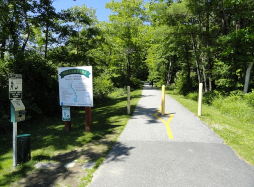 A paved path through a park, with a sign for Miller Park and trees lining the sides.