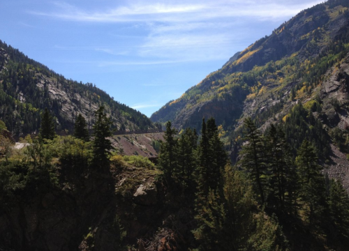 A scenic view of mountains with green trees and autumn foliage under a clear blue sky.