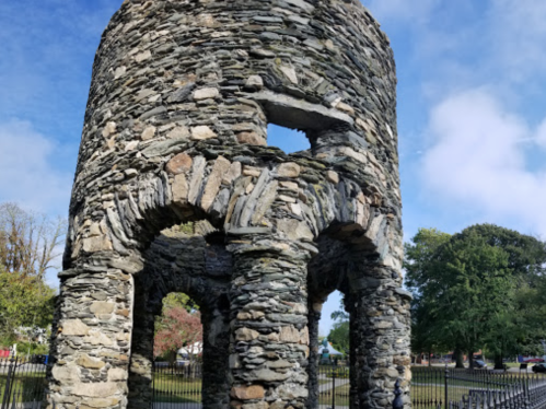 A stone structure with arched openings, surrounded by greenery and a blue sky.