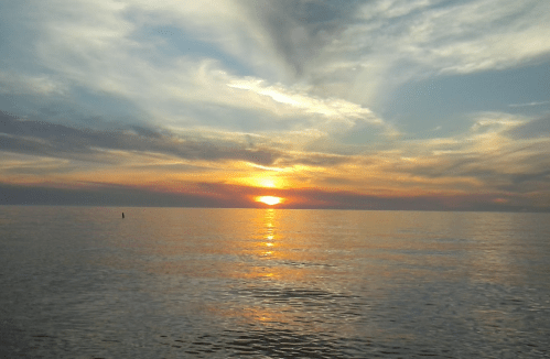 A serene sunset over calm waters, with vibrant orange and blue hues reflecting on the surface.