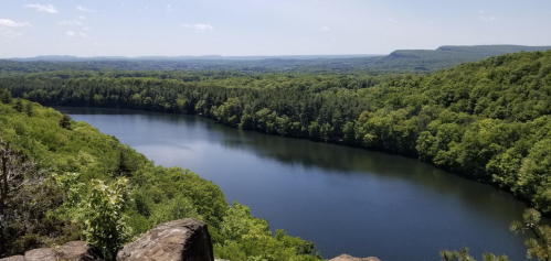 A serene view of a river surrounded by lush green trees and rolling hills under a clear blue sky.