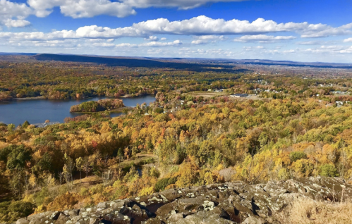 A scenic view of colorful autumn foliage, lakes, and rolling hills under a blue sky with fluffy clouds.