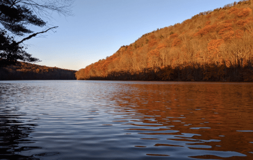 A serene lake surrounded by autumn trees, reflecting warm colors under a clear blue sky.