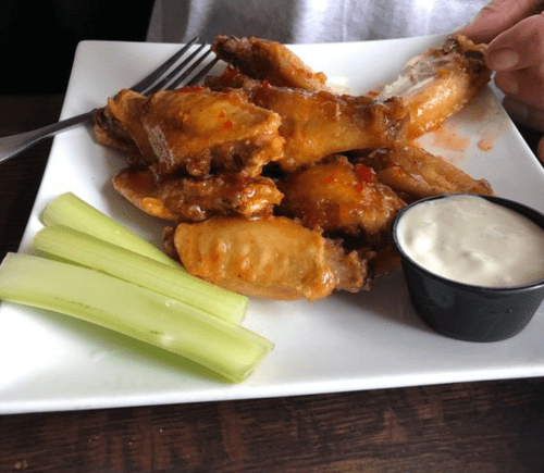 A plate of chicken wings glazed with sauce, served with celery sticks and a small cup of ranch dressing.