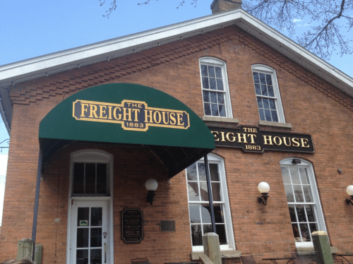 Exterior of The Freight House, a brick building with a green awning, featuring a sign with the year 1883.