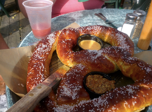 A large, soft pretzel with coarse salt, served with mustard and cheese dips on a table.