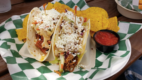 Two tacos filled with shredded meat, topped with lettuce and cheese, served with tortilla chips and salsa on the side.