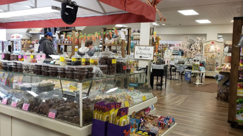 A colorful candy shop display with jars of sweets and treats, and shoppers browsing in a cozy, inviting store.