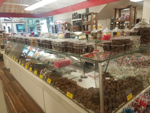 A colorful candy shop display featuring various jars of chocolates, gummies, and sweets in a glass case.