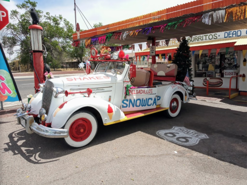 A colorful vintage truck decorated with festive elements, parked outside a retro diner on Route 66.
