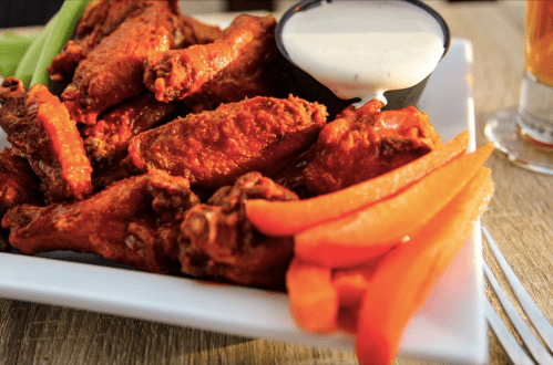 A plate of spicy chicken wings with a side of ranch dressing and carrot sticks, served on a wooden table.