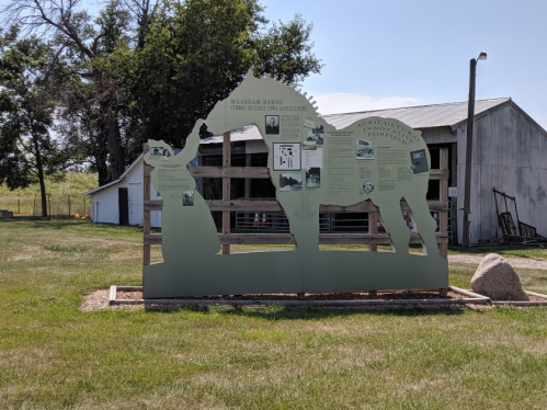 A large silhouette of a horse with informational panels about agriculture, set in a grassy area near a barn.