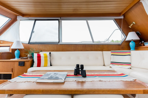 Cozy boat interior featuring a white sofa, colorful striped pillows, a wooden table, and binoculars on a magazine.