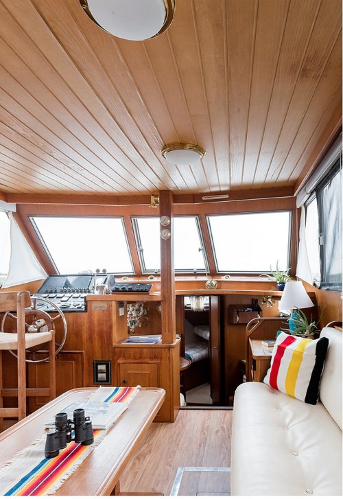 Interior of a boat featuring wooden paneling, a cozy seating area, and a navigation station with large windows.