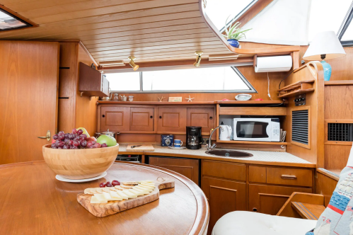 Cozy boat interior featuring a wooden kitchen with a bowl of grapes, cheese platter, and modern appliances.