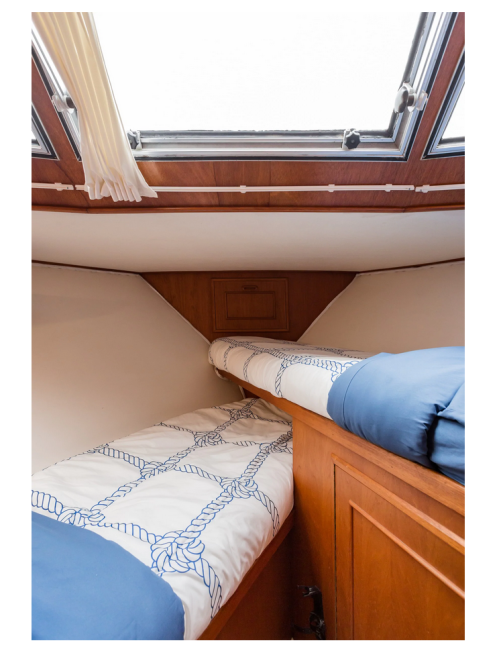 Cozy interior of a boat cabin featuring two beds with nautical-themed bedding and a skylight above.