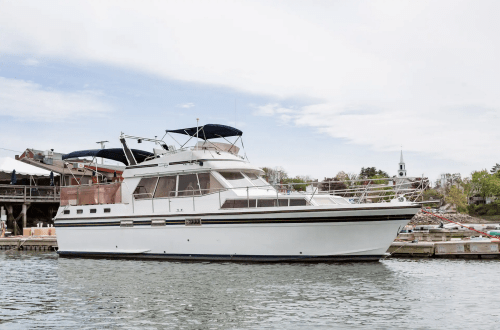 A white motor yacht docked at a marina, with a blue sky and a church steeple visible in the background.