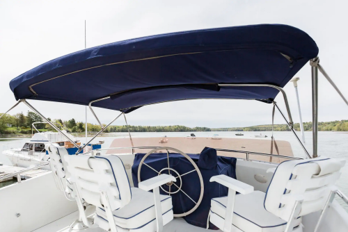 View from the back of a boat featuring a blue canopy, white seating, and a scenic water landscape with boats.
