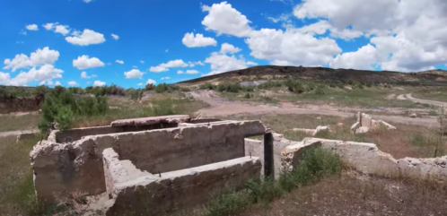 Ruins of a stone structure in a grassy landscape under a bright blue sky with fluffy clouds.