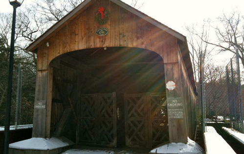 A wooden covered bridge with a wreath, featuring "No Smoking" signs, surrounded by snow and trees.