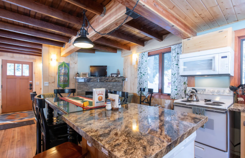 Cozy kitchen with wooden beams, granite countertops, a stone fireplace, and modern appliances in a rustic setting.
