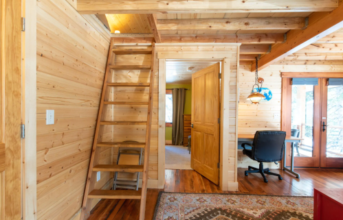 Interior of a wooden cabin featuring a staircase, doorways, and a cozy workspace with natural light.