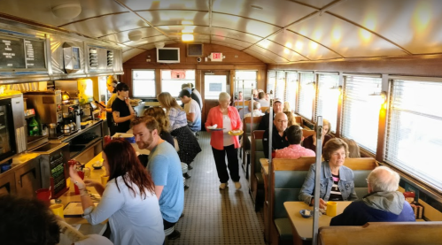 A busy diner interior with patrons seated at booths, enjoying meals and drinks, and staff serving food.