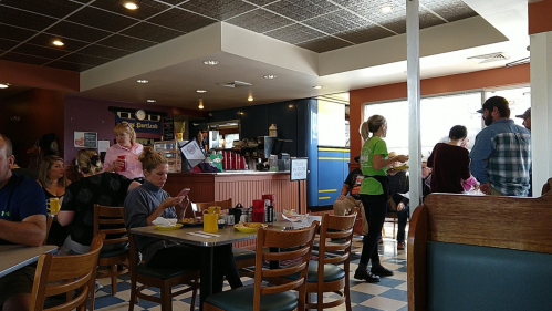 A busy diner scene with patrons eating, a waitress serving, and a colorful interior featuring checkered floors.