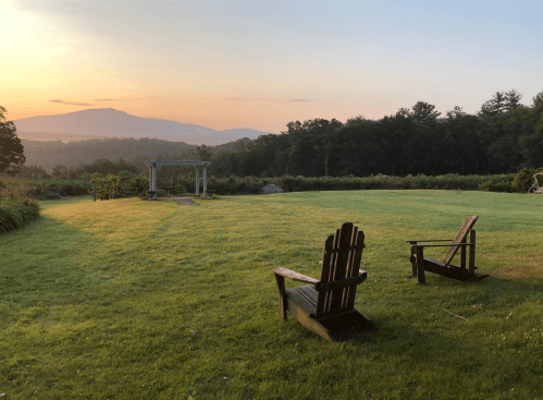 Two wooden rocking chairs on a grassy lawn, with a sunset over mountains in the background.