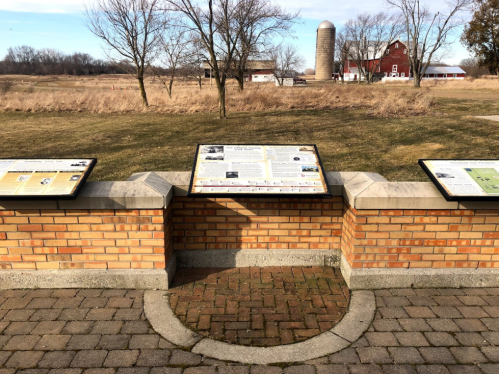 Informational panels on a brick structure with a rural landscape and a red barn in the background.