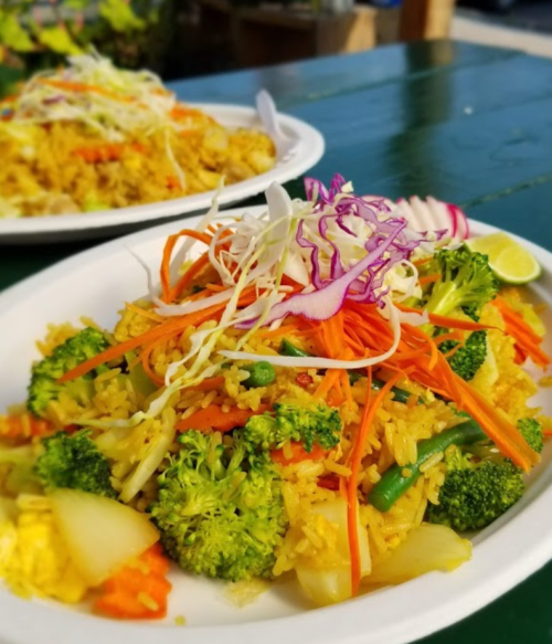 A colorful plate of vegetable fried rice topped with shredded cabbage, carrots, and lime, served on a white platter.
