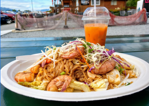 A plate of shrimp stir-fried noodles topped with cabbage and herbs, alongside a cup of iced tea.