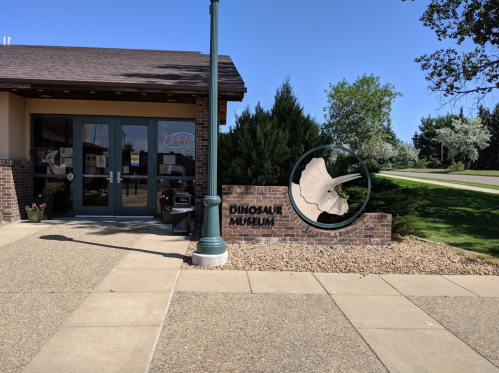 Exterior of a Dinosaur Museum with a sign featuring a dinosaur fossil and an "OPEN" sign on a clear day.