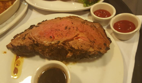 A succulent slice of prime rib served on a plate with two small bowls of sauce on the side.