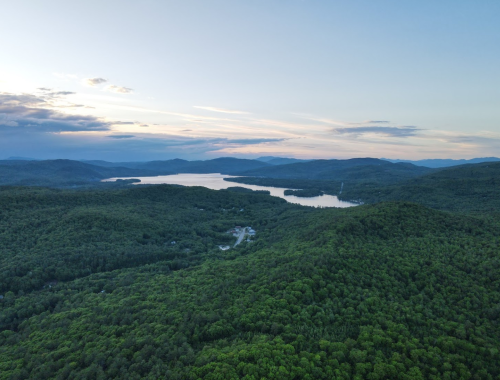 Aerial view of lush green mountains surrounding a serene lake under a clear sky at sunset.