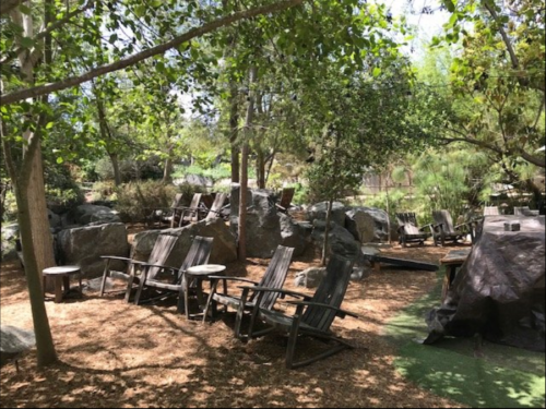 A serene outdoor space with wooden chairs, rocks, and trees, creating a peaceful, natural setting.