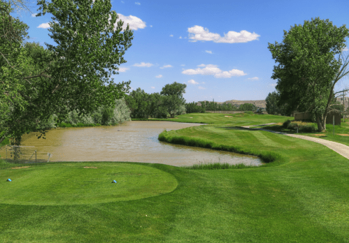A scenic golf course with lush green grass, a winding river, and blue skies dotted with clouds.