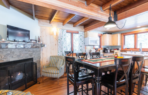 Cozy kitchen with wooden beams, stone fireplace, dining table, and large windows letting in natural light.