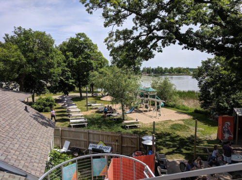 A scenic view of a park with picnic tables, a playground, and a lake in the background, surrounded by trees.