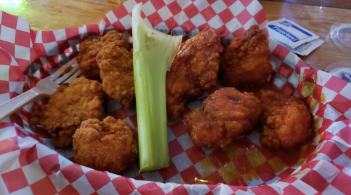 A plate of crispy fried chicken wings with a celery stick, served in a red and white checkered basket.