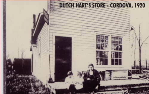 Historic black-and-white photo of Dutch Hart's Store in Cordova, 1920, with a woman and two children seated outside.